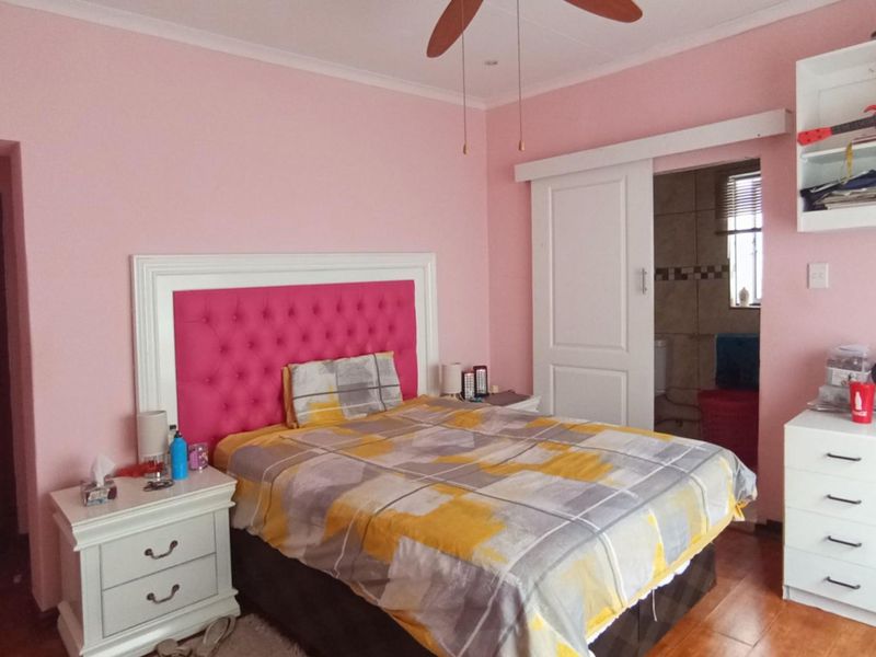 A bedroom featuring hardwood flooring, a ceiling fan, and a sliding door leading to an en-suite bathroom with built-in shelving.
