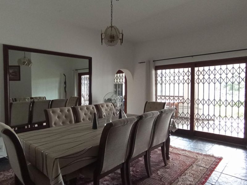 Spacious dining room featuring slate tile flooring, a large wall mirror, and sliding glass doors with security gates leading to the outdoor area.