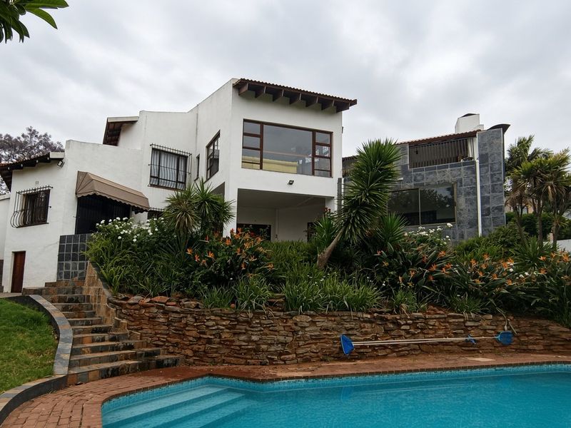 Rear view of the multi-level residence featuring a swimming pool, stone retaining wall, landscaped garden, and a spacious balcony.