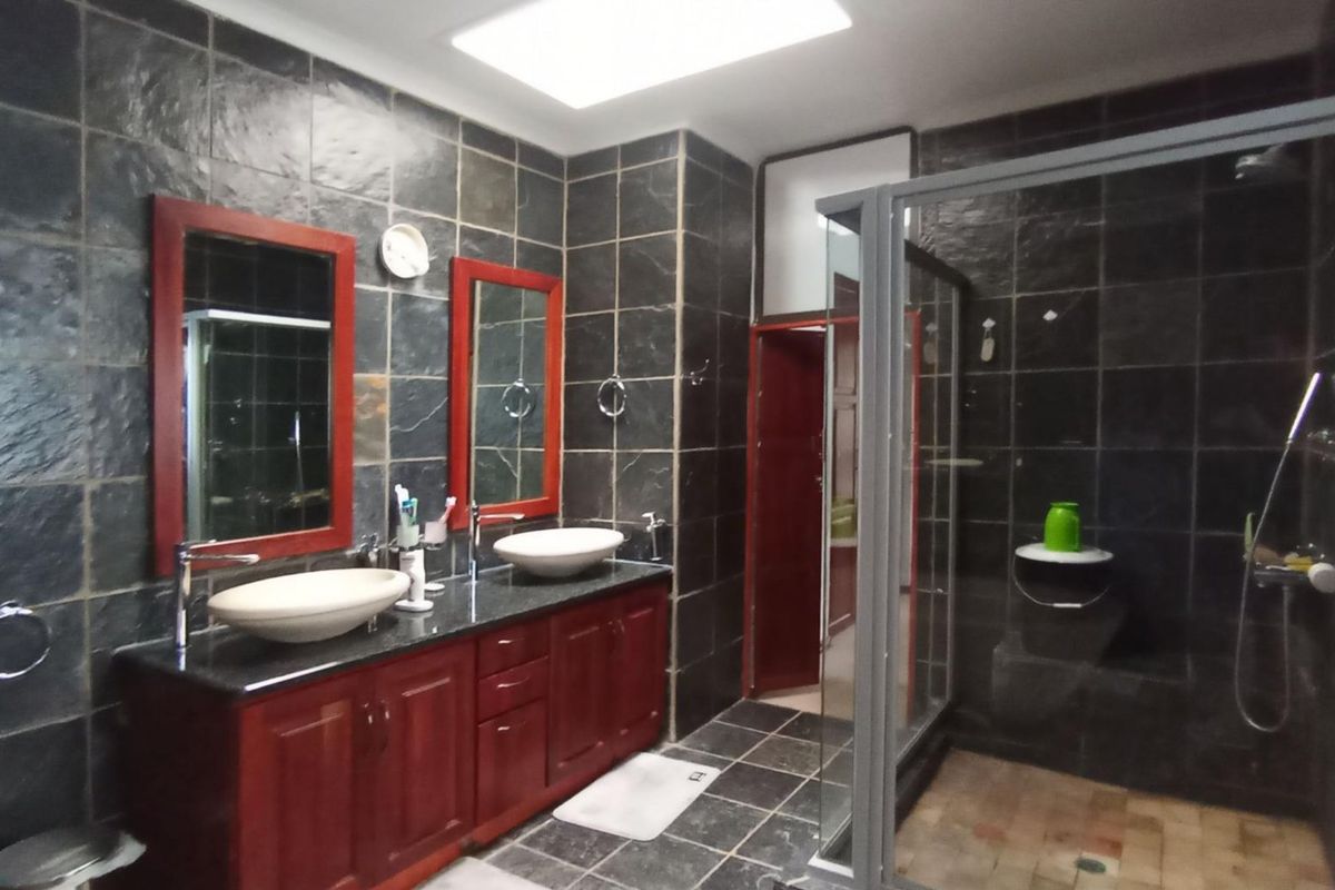A spacious bathroom featuring a double vanity with vessel sinks, granite countertops, and a walk-in shower, finished with dark slate wall tiles and a skylight.