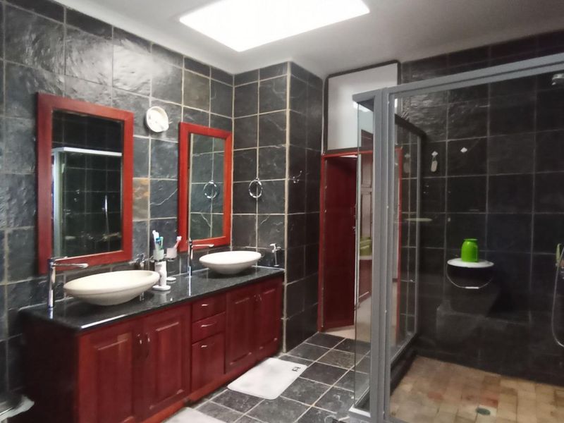 A spacious bathroom featuring a double vanity with vessel sinks, granite countertops, and a walk-in shower, finished with dark slate wall tiles and a skylight.