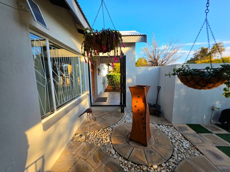 A well-maintained front entrance courtyard featuring paved stone pathways, decorative pebble landscaping, and secure window bars.