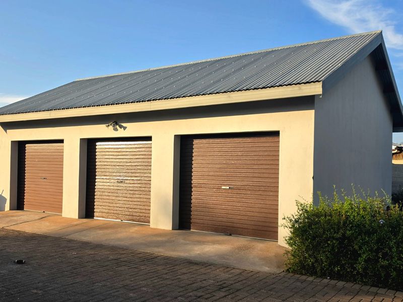 A detached triple garage featuring brown roller doors, a corrugated metal roof, and a paved driveway area.