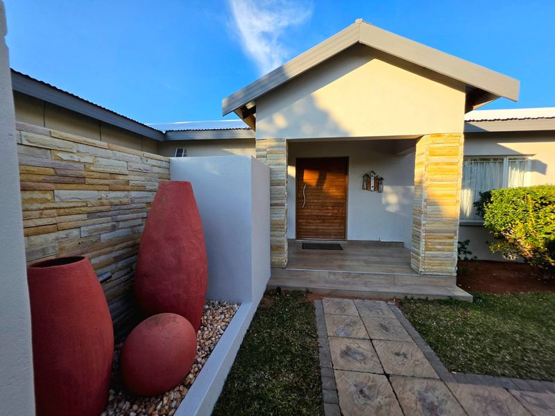 A well-maintained front entrance featuring stone cladding accents, a modern timber door, and a paved walkway leading to a covered porch.