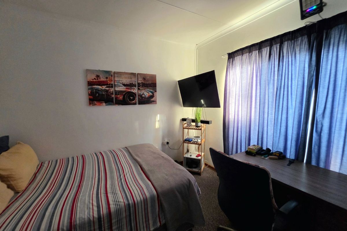 A functional bedroom featuring carpeted flooring and window treatments, providing a comfortable space for rest and study.
