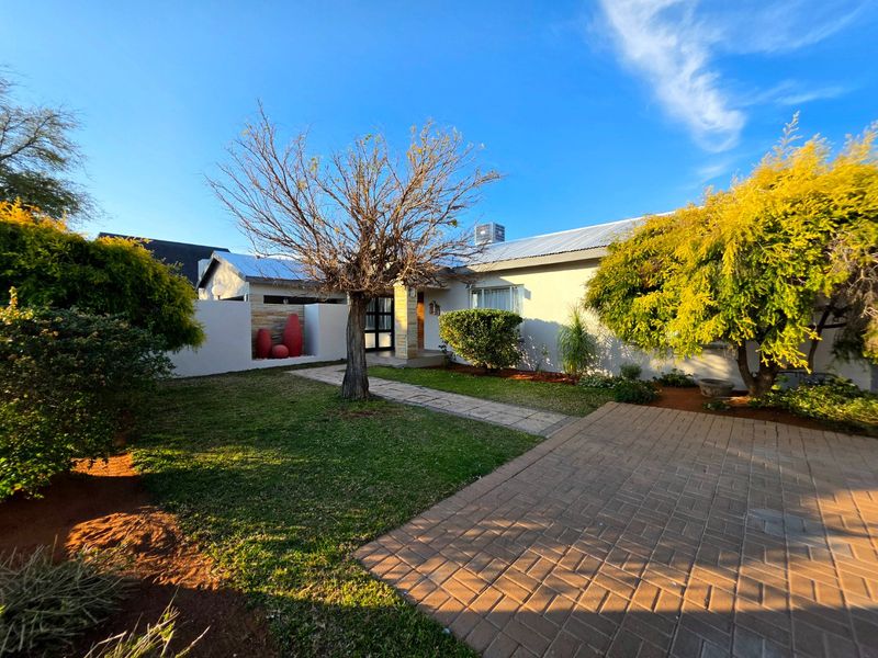 Front view of the house featuring a paved driveway, stone walkway, and landscaped garden area with established trees.