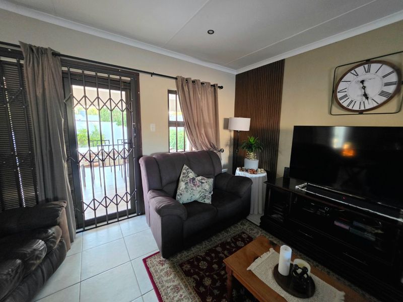 A comfortable living room featuring tiled flooring, recessed lighting, and a decorative timber wall panel, with direct access to an outdoor patio area.