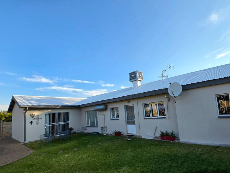 Rear view of the house featuring a corrugated metal roof, security bars on windows, and a small lawn area.