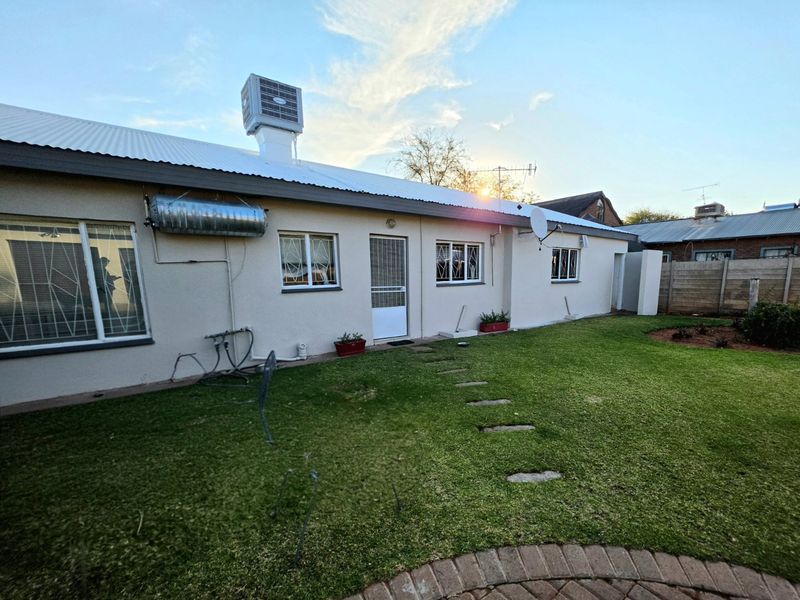 Rear view of the property featuring a lawn, paved walkway, and exterior building infrastructure including a solar water heater and roof-mounted cooling unit.