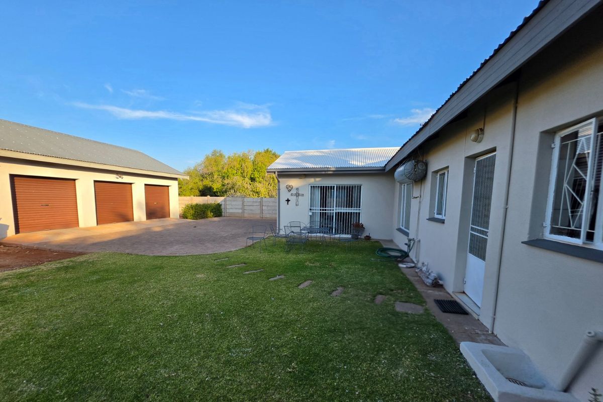 Rear view of the property featuring a well-maintained lawn, paved driveway, and a triple garage with roll-up doors.