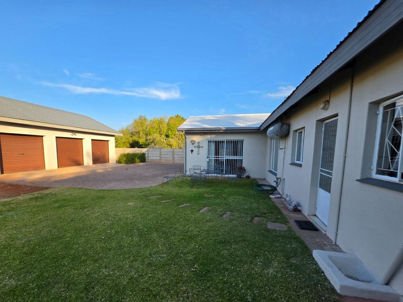 Rear view of the property featuring a well-maintained lawn, paved driveway, and a triple garage with roll-up doors.