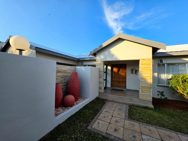 A well-maintained front entrance featuring stone cladding accents, a modern timber door, and a paved walkway leading to a tiled porch area.