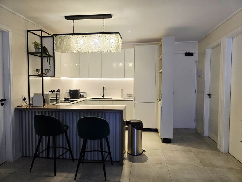 Modern kitchen featuring sleek white cabinetry, under-cabinet lighting, a functional island with breakfast bar seating, and contemporary tiled flooring.