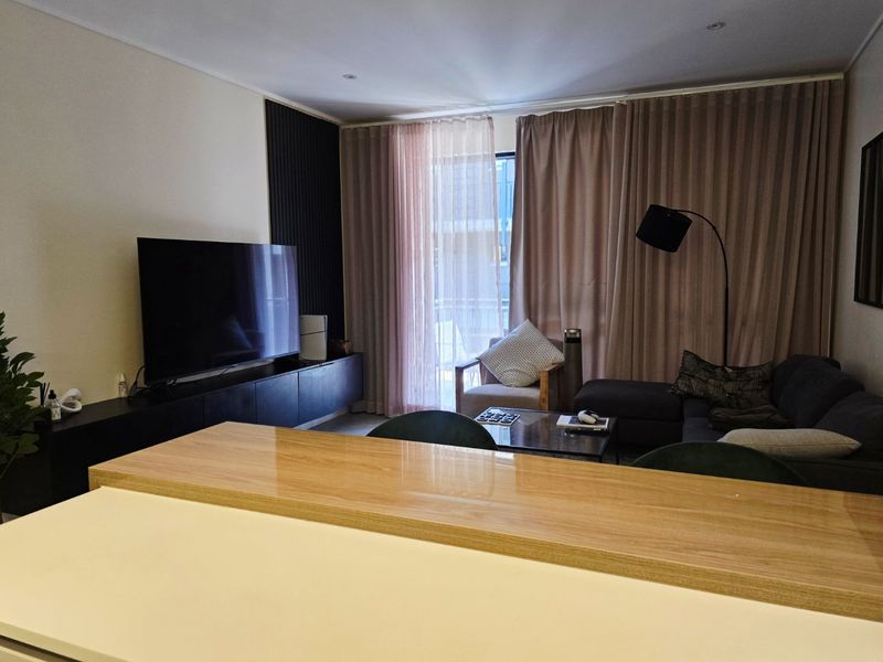 Modern open-plan living area featuring a breakfast bar, slatted feature wall, and direct access to a balcony through sliding glass doors.