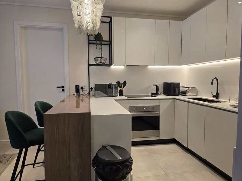Modern kitchen featuring sleek white cabinetry, stone countertops, a breakfast bar, integrated appliances, and contemporary black fixtures with under-cabinet lighting.