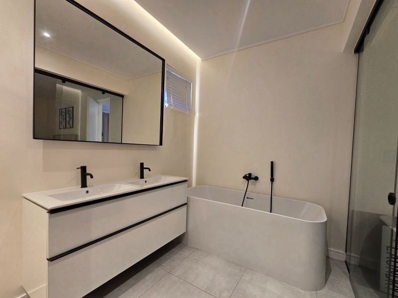 Modern bathroom featuring a sleek double vanity with black matte fixtures, a contemporary freestanding bathtub, and elegant recessed lighting.