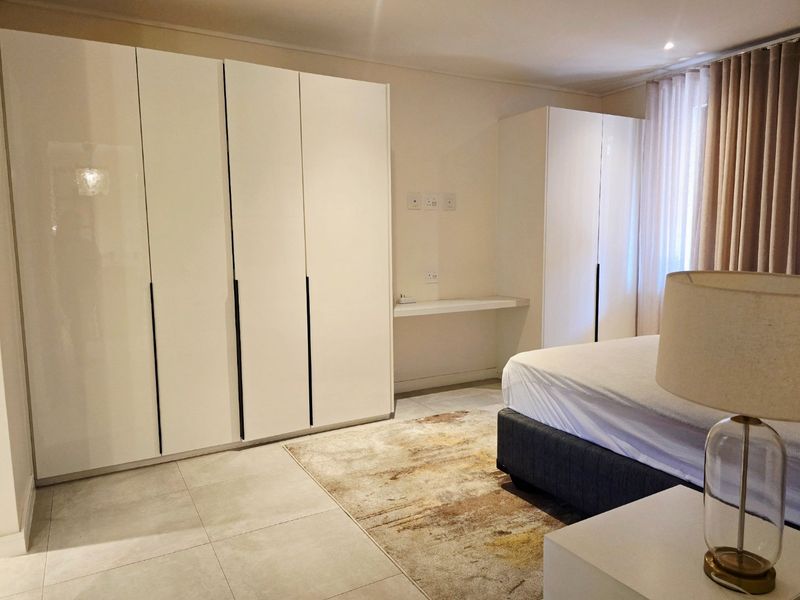 A well-maintained bedroom featuring modern high-gloss built-in cupboards, a floating desk area, and neutral tiled flooring.