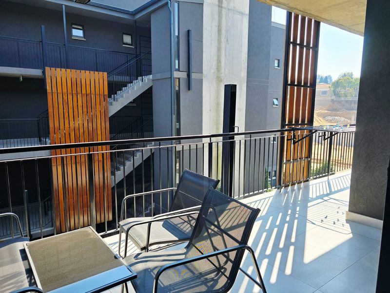 A modern covered balcony featuring tiled flooring, a metal balustrade, and decorative timber slat privacy screens overlooking the apartment complex exterior.