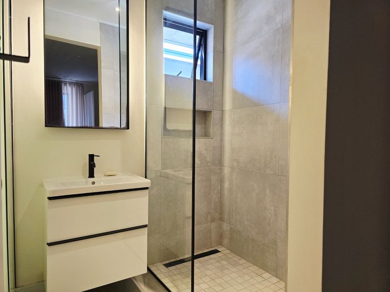 Modern bathroom featuring a wall-mounted vanity with black fixtures, a walk-in shower with a recessed niche, and contemporary grey tiling.