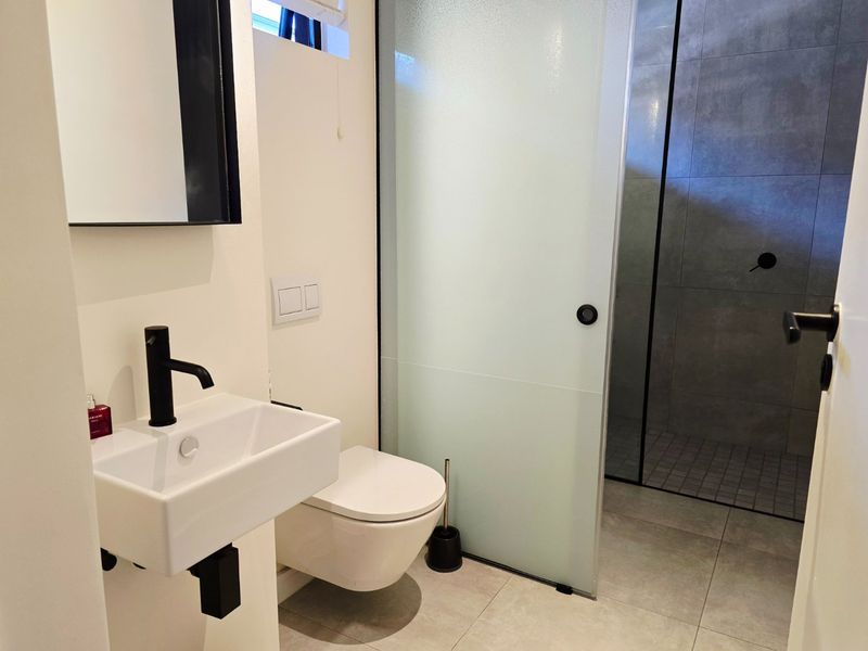Modern bathroom featuring a wall-mounted basin with black fixtures, a wall-hung toilet, and a spacious walk-in shower with a frosted glass door.