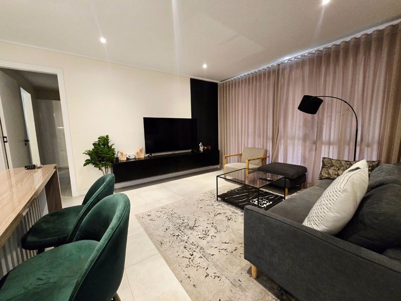 Modern open-plan living area featuring tiled flooring, recessed downlighting, and a sleek built-in media console with decorative slatted wall paneling.