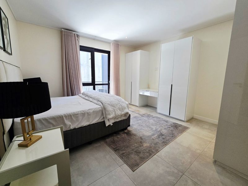 A well-maintained bedroom featuring neutral tiled flooring, built-in cupboards with a vanity section, and direct access to a balcony through sliding doors.
