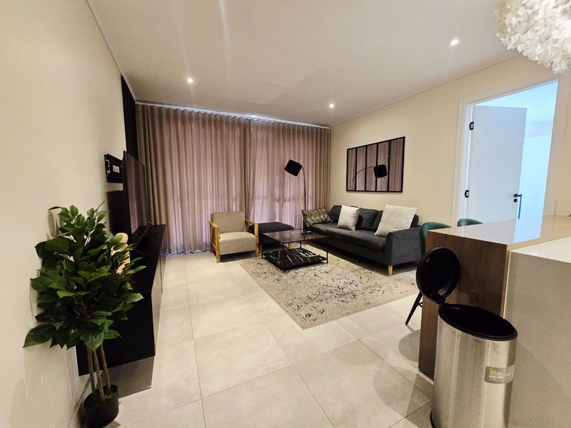 A well-maintained living room featuring neutral tiled flooring and recessed downlighting, creating a bright and comfortable atmosphere.
