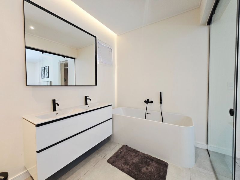 Modern bathroom featuring a sleek double vanity with black matte fixtures, a contemporary freestanding bathtub, and clean tiled finishes.