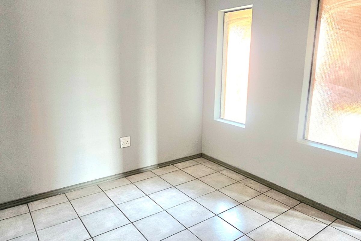 A vacant bedroom featuring neutral tiled flooring, clean walls, and two windows with an installed curtain track.