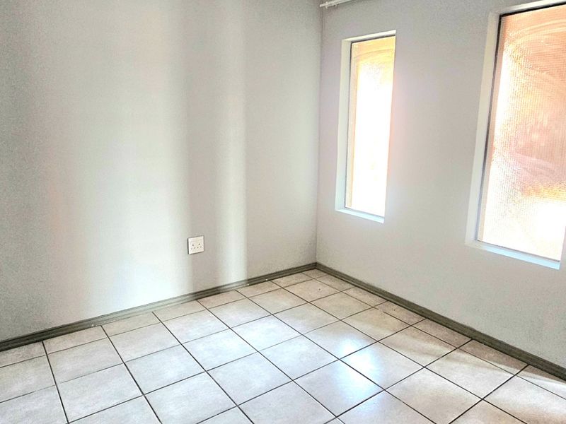 A vacant bedroom featuring neutral tiled flooring, clean walls, and two windows with an installed curtain track.