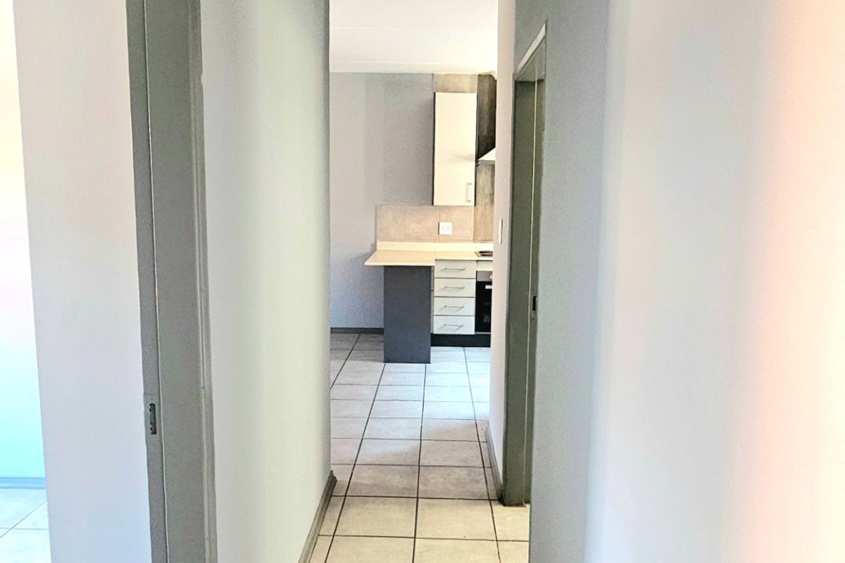 A clean, neutral-toned hallway with tiled flooring, providing access to adjacent rooms and a view into the kitchen area.