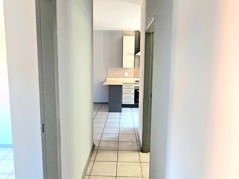 A clean, neutral-toned hallway with tiled flooring, providing access to adjacent rooms and a view into the kitchen area.