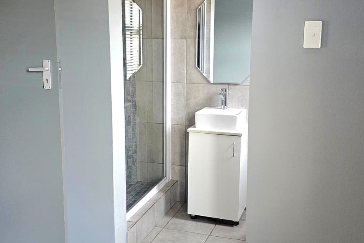 A clean, functional bathroom featuring a shower enclosure, a modern vanity with basin, and neutral wall and floor tiling.