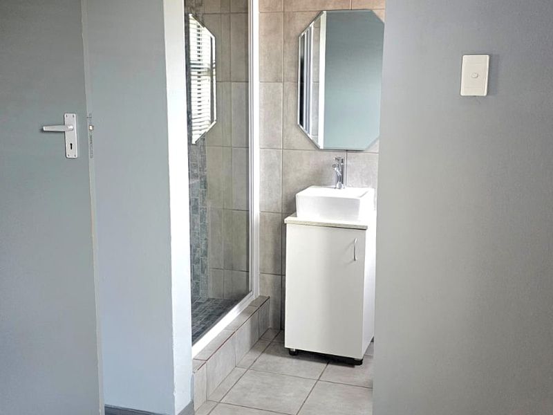 A clean, functional bathroom featuring a shower enclosure, a modern vanity with basin, and neutral wall and floor tiling.