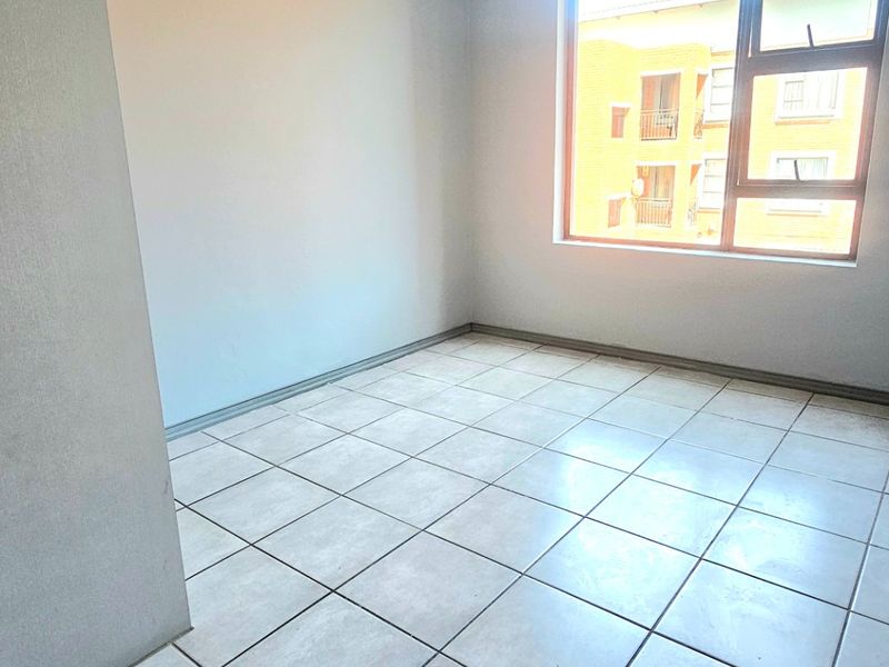 A bright, empty bedroom featuring neutral tiled flooring and a large aluminium-framed window, providing a clean and versatile space ready for personalization.