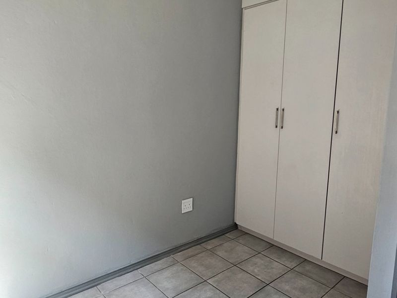 A clean, empty bedroom featuring neutral grey walls, tiled flooring, and built-in storage cupboards.