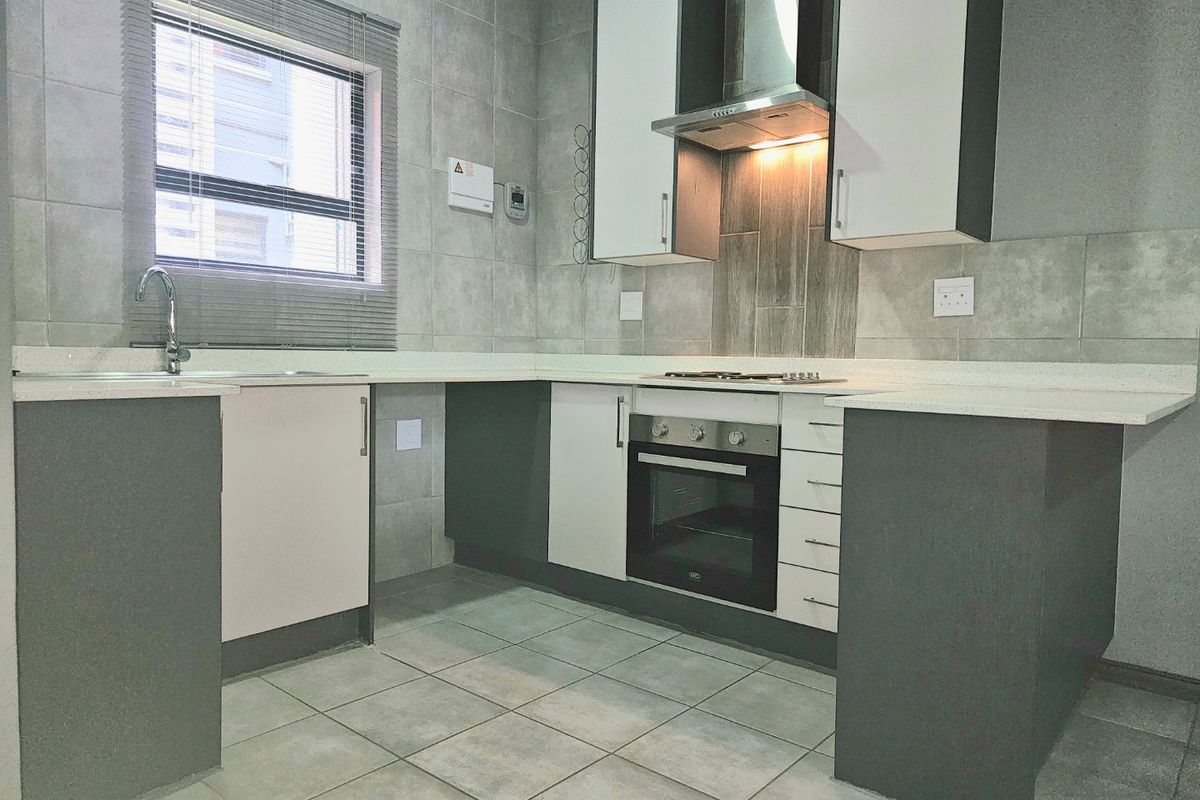 A modern, well-maintained kitchen featuring sleek built-in cabinetry, stone countertops, integrated oven and hob, and neutral tiled finishes throughout.