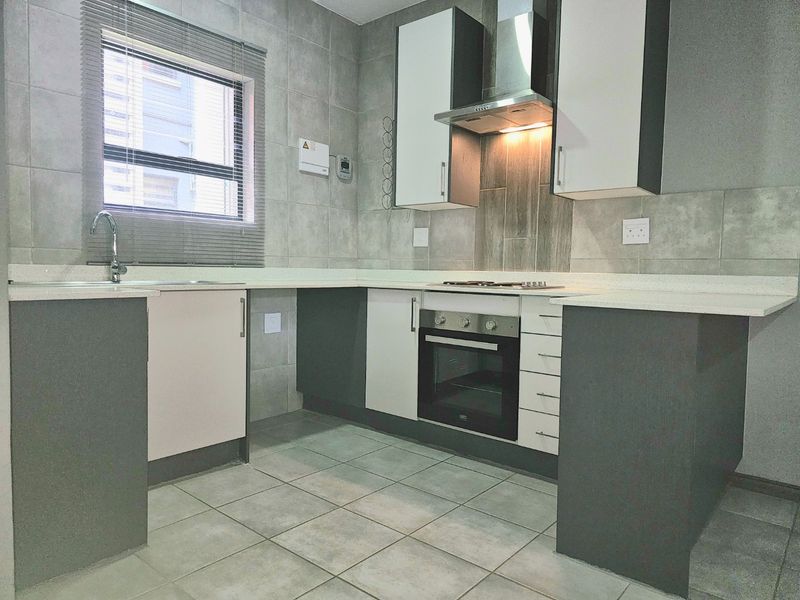 A modern, well-maintained kitchen featuring sleek built-in cabinetry, stone countertops, integrated oven and hob, and neutral tiled finishes throughout.