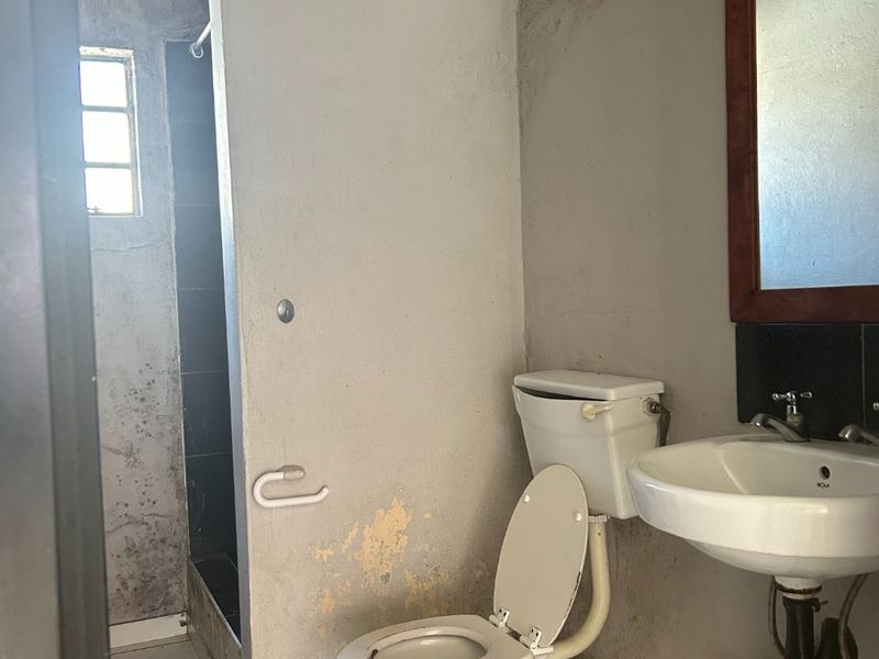 A dated bathroom featuring a pedestal basin, toilet, and shower enclosure, currently requiring significant renovation and repair to the walls and finishes.