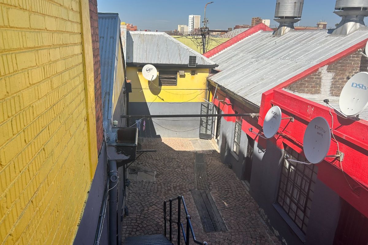 Rear exterior courtyard area featuring cobblestone paving, metal staircase access, and multiple satellite dishes mounted on painted brick walls with corrugated metal roofing.