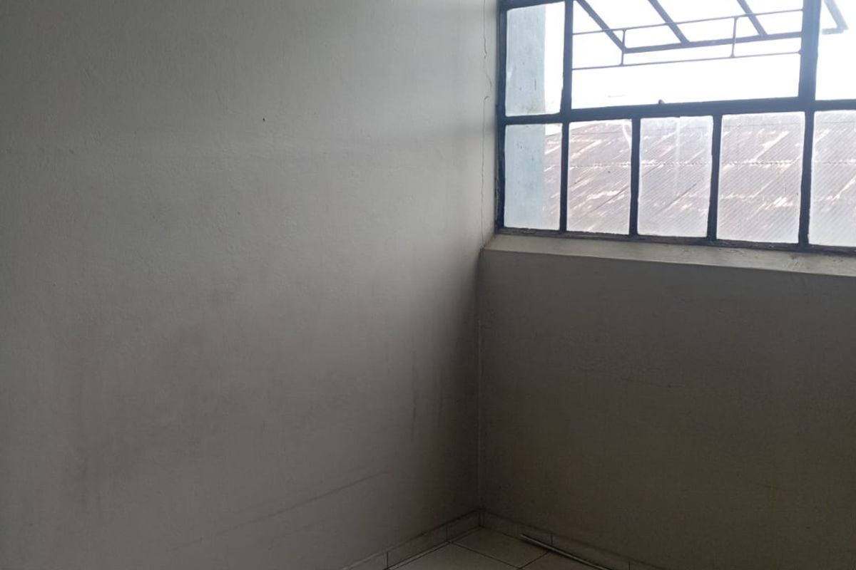 An empty, compact room featuring tiled flooring and a large steel-framed window, requiring cosmetic updates to improve its overall condition and appeal.