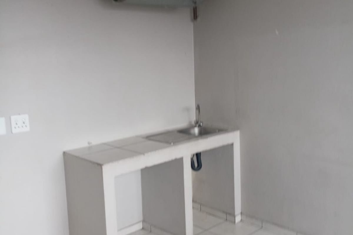 A basic utility kitchen area featuring a tiled counter with a sink and a wall-mounted electric geyser.