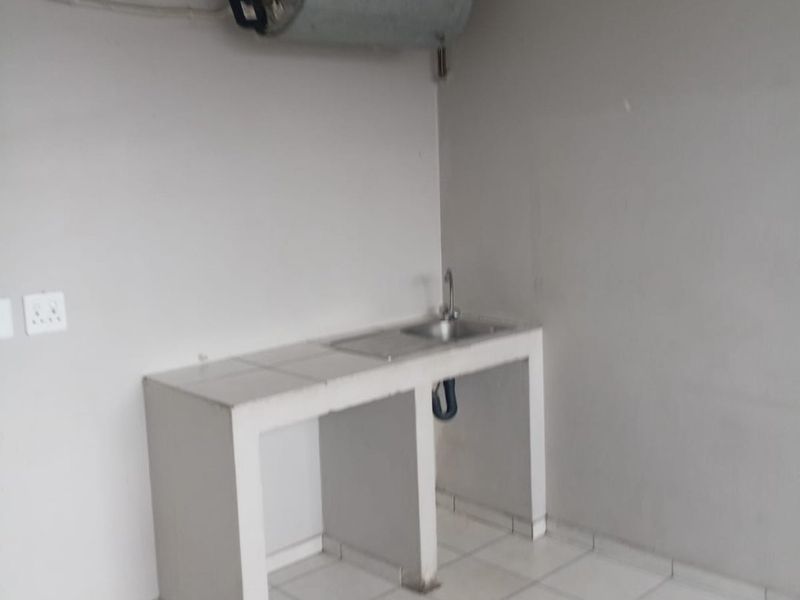 A basic utility kitchen area featuring a tiled counter with a sink and a wall-mounted electric geyser.