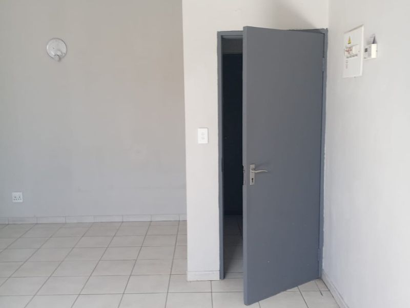 A vacant, neutral-toned office space featuring tiled flooring, a grey interior door, and basic electrical infrastructure.
