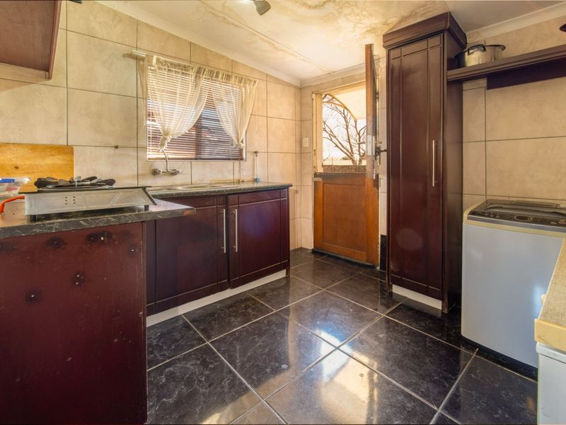 A functional kitchen featuring dark cabinetry, tiled surfaces, and a stable door leading to the exterior, showing signs of ceiling water damage.