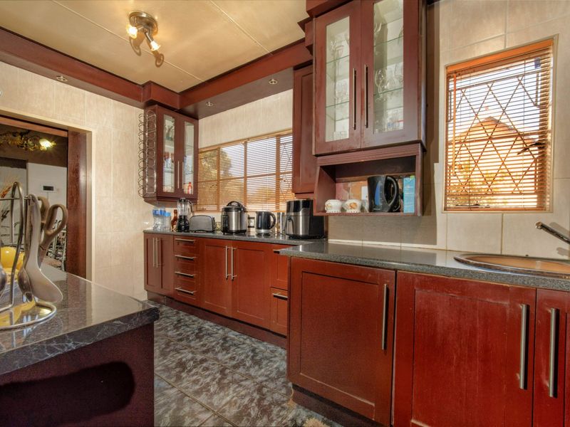 A functional kitchen featuring dark wood cabinetry, granite countertops, tiled backsplash, and tiled flooring with ample storage and integrated sink.