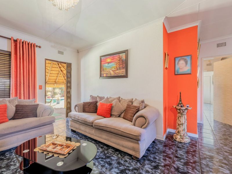 A living room featuring dark tiled flooring, a bright orange accent wall, and a sliding door providing access to an outdoor area.