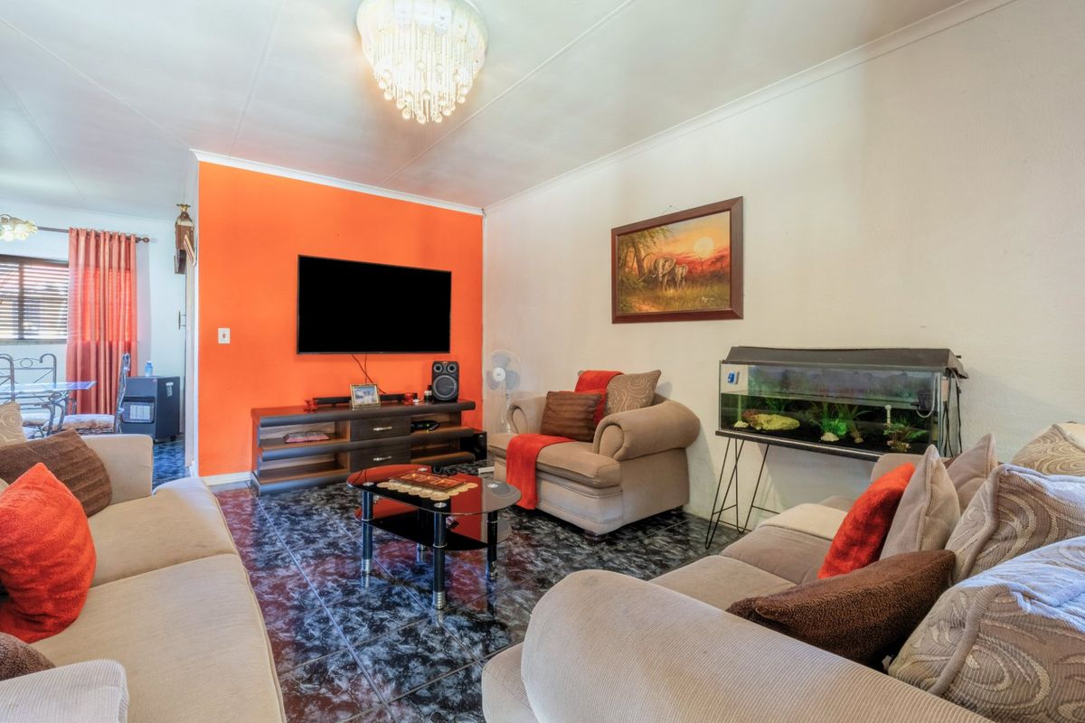 A living room featuring tiled flooring, a coved ceiling, and a central crystal chandelier, with a vibrant orange accent wall.