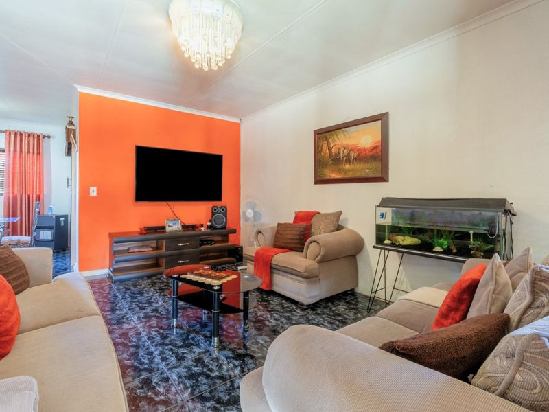 A living room featuring tiled flooring, a coved ceiling, and a central crystal chandelier, with a vibrant orange accent wall.