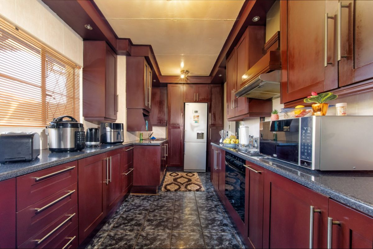 A galley-style kitchen featuring dark wood cabinetry, laminate countertops, built-in oven, extractor fan, and tiled flooring.